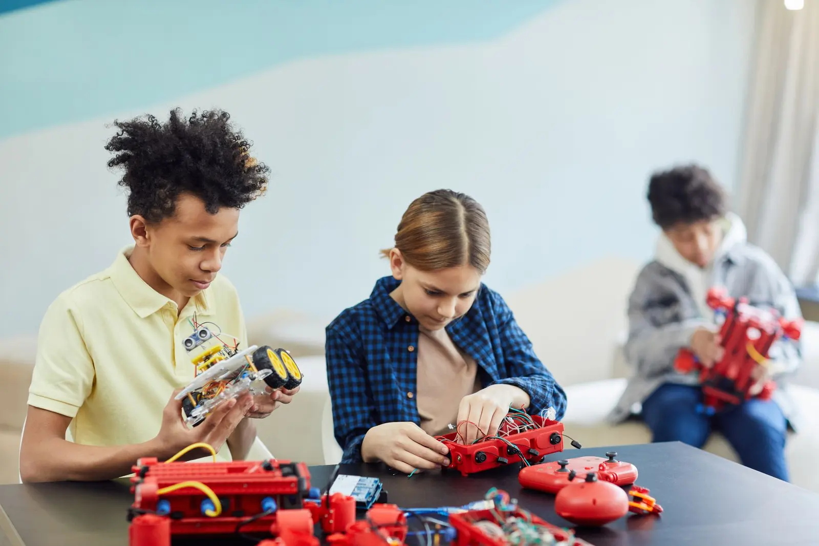 Three teenagers building small robots at a table.